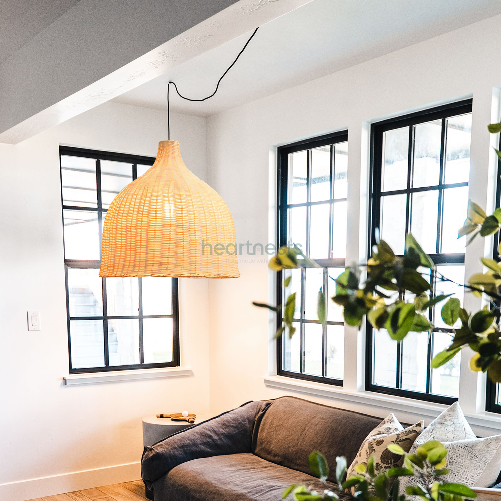 1 of Heart Nests's Baleria wicker hanging light with light on are hung over a leather couch next to a big black frame window