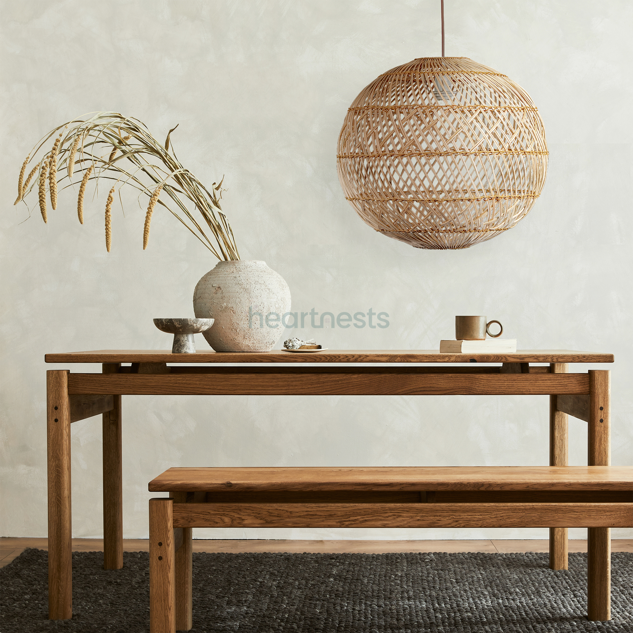A Ballia round shape rattan pendant lights with lights on from brand Heart Nestsare hung above a wooden table with a wooden bench