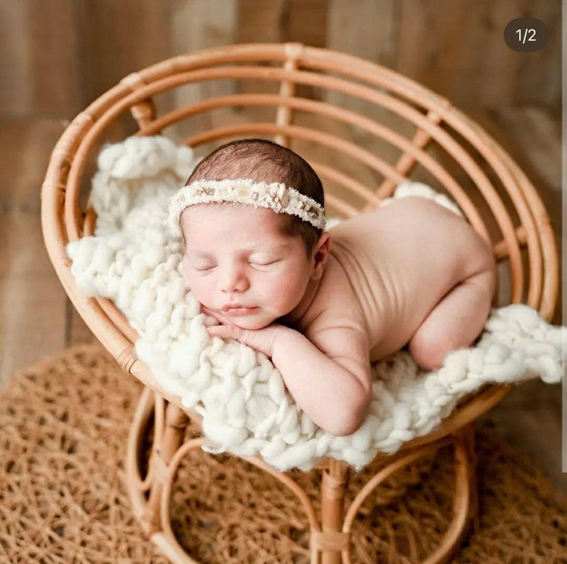 A Heartnests' Molisa Rattan Baby Parpasan Chair for Baby Photography with a layer of white macrame and baby sleeping on it is placed on a natural jute color flower shape rug