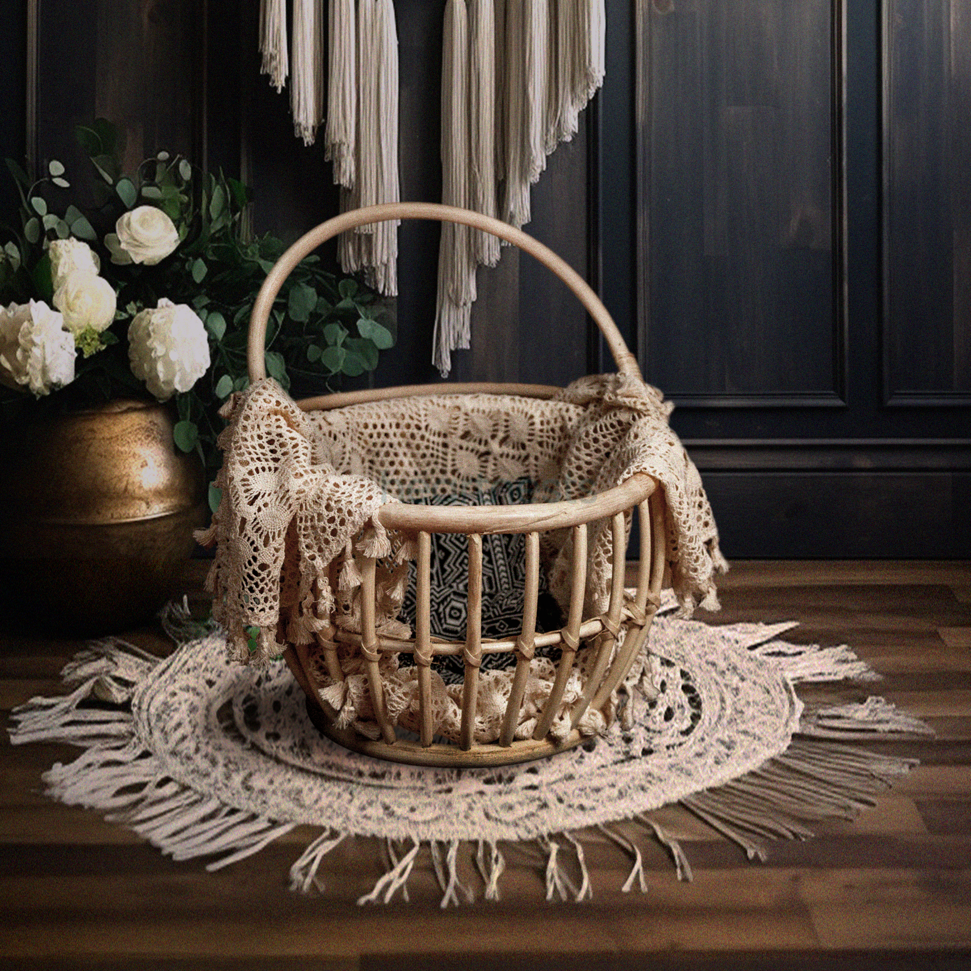 A Heartnests' Kira Rattan Baby Photography Basket with handles is placed on a circular shape white macrame on dark brown wooden flooring and in front of a white macrame and a seagrass flower basket
