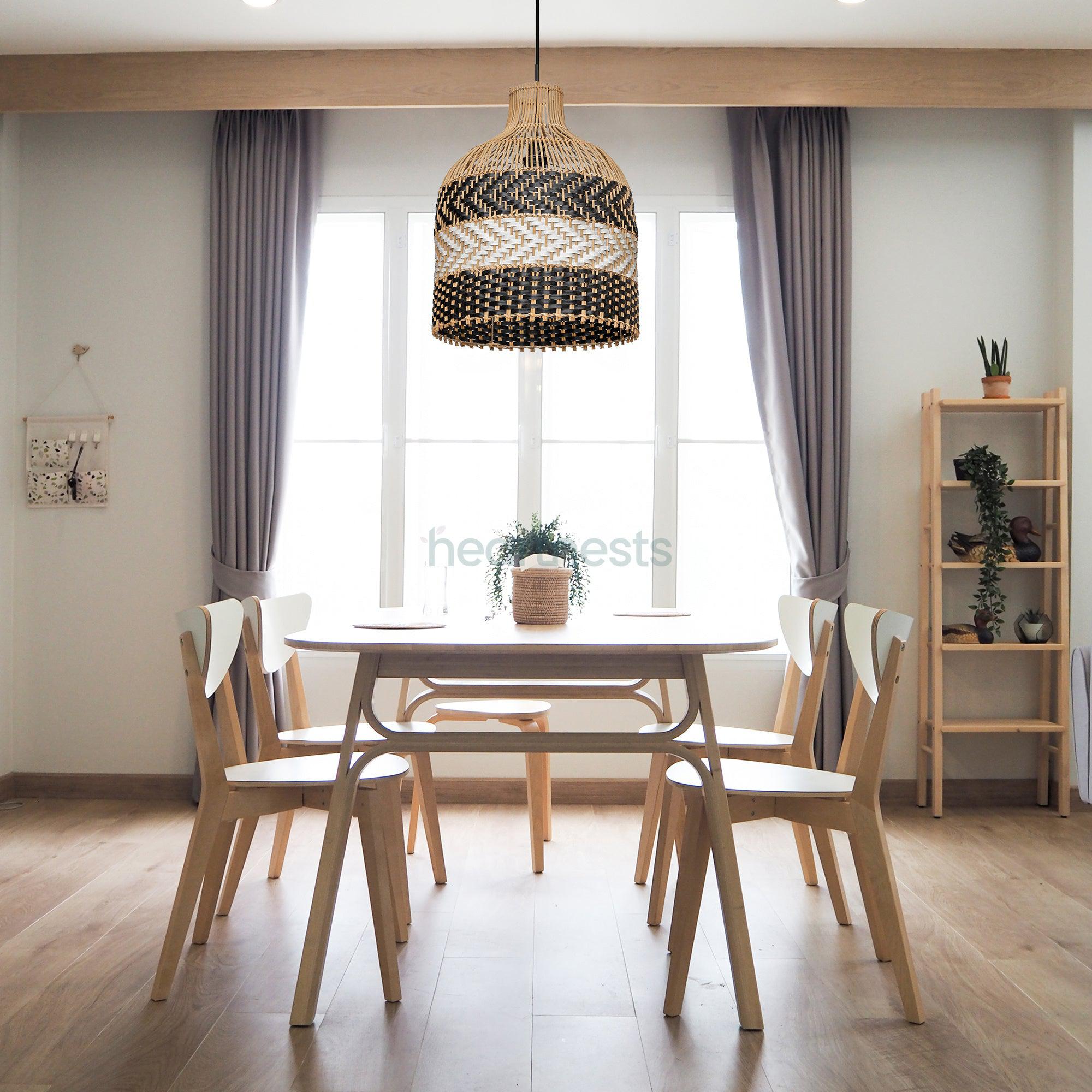 A Heartnests' Luka Wicker Pendant Light is hung above a wooden living room table with 2 wooden chairs in a minimalistic style living room