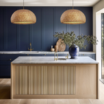 2 Heart Nests's Alinta bamboo pendant lights are hung side by side above a wooden kitchen island. The kitchen wall is a featured panel wall in blue hue