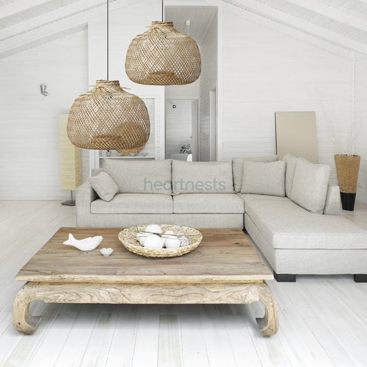 2 Bali bamboo pendant lights from brand Heart Nests are hung in different heights above a wooden natural tone living room table and a light gray cloud chase sofa following coastal rustic style