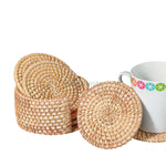 An arrangement of a  white glass placed on a Heartnests's Costella Rattan Coaster next to a coaster holder