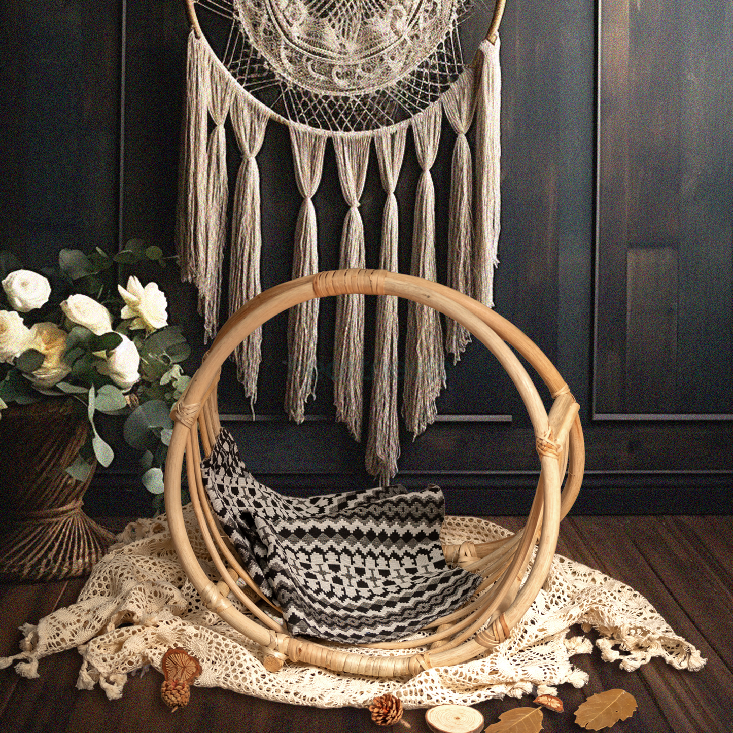 A Heartnests's Rattan Baby Prop is placed on a white macrame and in front of a white dream catcher next to a beautiful white flower vase