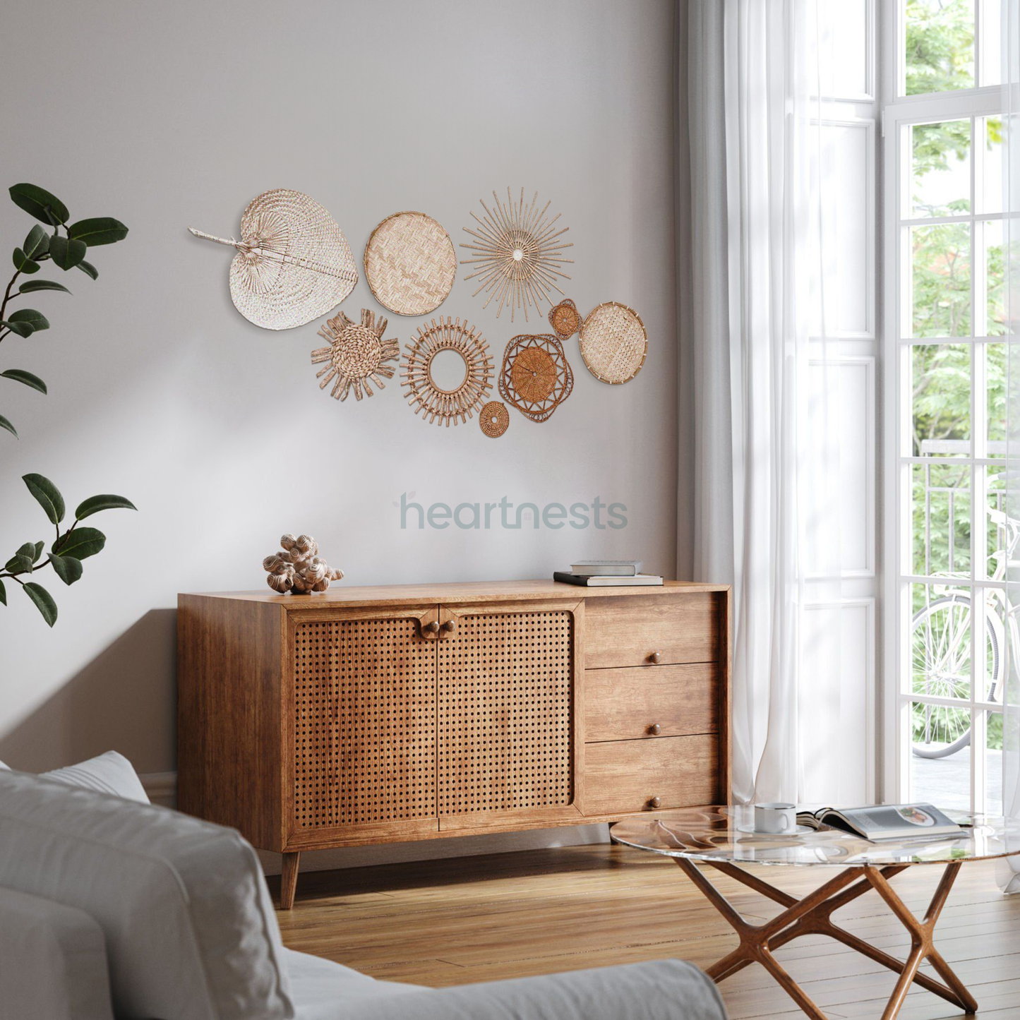 A set of Heartnests' 9 Freiya rattan and seagrass wall decor are hung above a brown wooden tall chest next to a large bright window