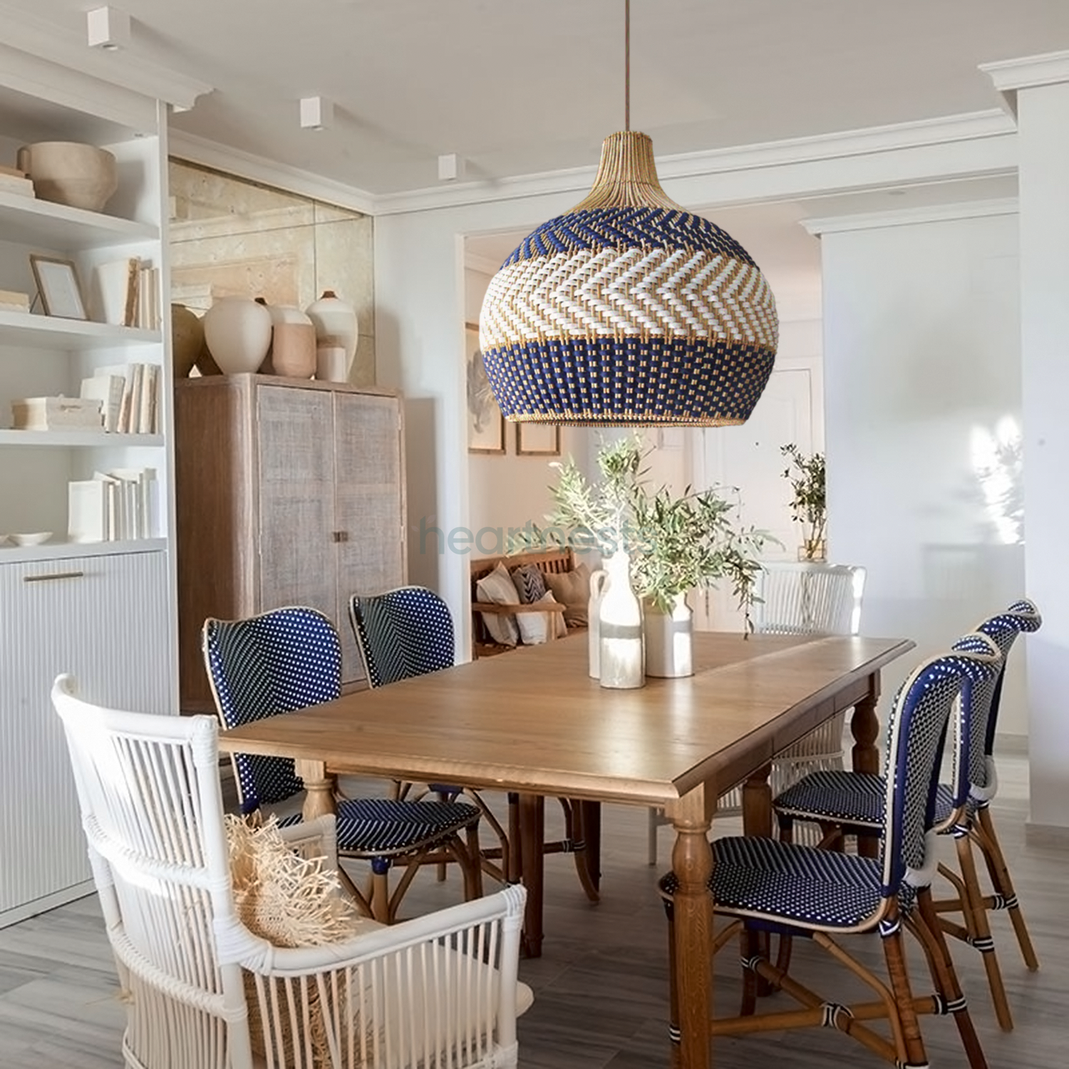 A Heartnests' Cosmo rattan pendant light is hung above a wooden dining room table with 5 dark tone wooden chairs and 1 white color wicker chair