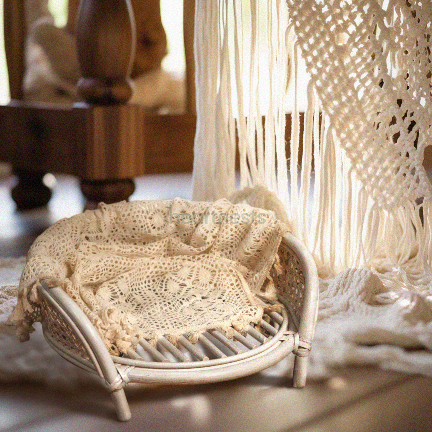 A Heartnests' Lilly Rattan Newborn Prop is on a dark flooring and in front of a large white macrame