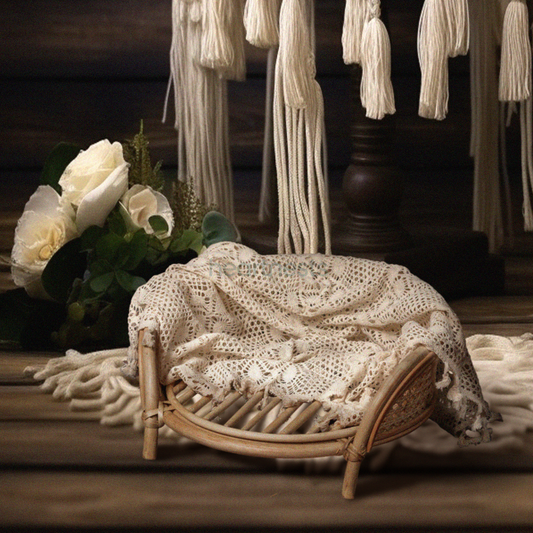 A Heartnests' Lilly Rattan Baby Prop in natural rattan colour is on dark brown wooden floor next to a flower basket and there's macrame tassels hung down from the wall behind the prop
