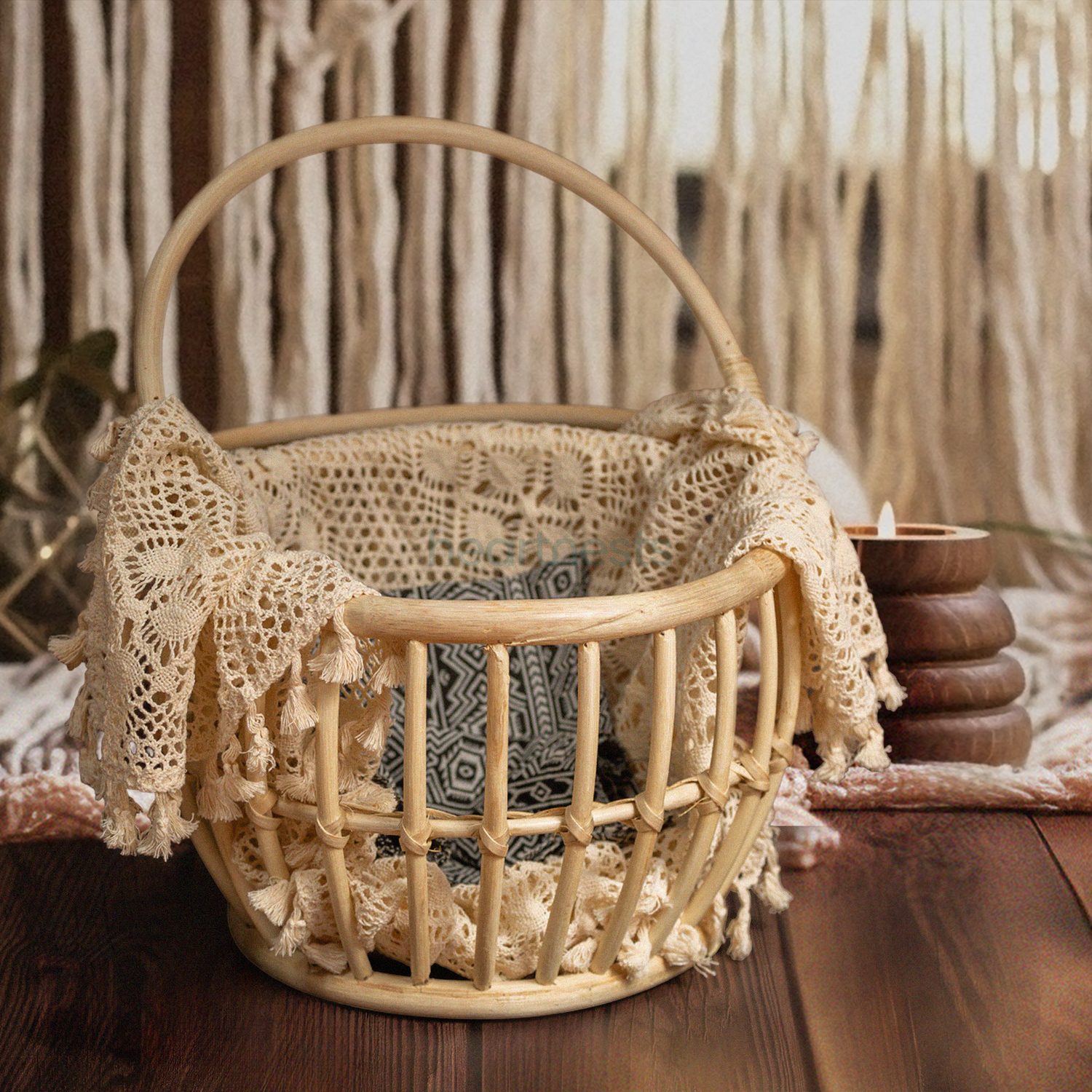 A Heartnests' Kira Rattan Baby Photography Basket with handles is placed on a dark brown wooden flooring and in front of a white macrame