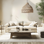 A Heartnests' Lombok Seagrass Wicker Pendant Light is hung above a wooden round table and a 3 seater light grey color sofa