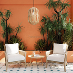 A Heartnests' Malee Rattan Pendant Light is hung above 2 rattan armchairs placed in front of a bright orange colour feature wall and an orange colour retainer with 2 big tropical green trees