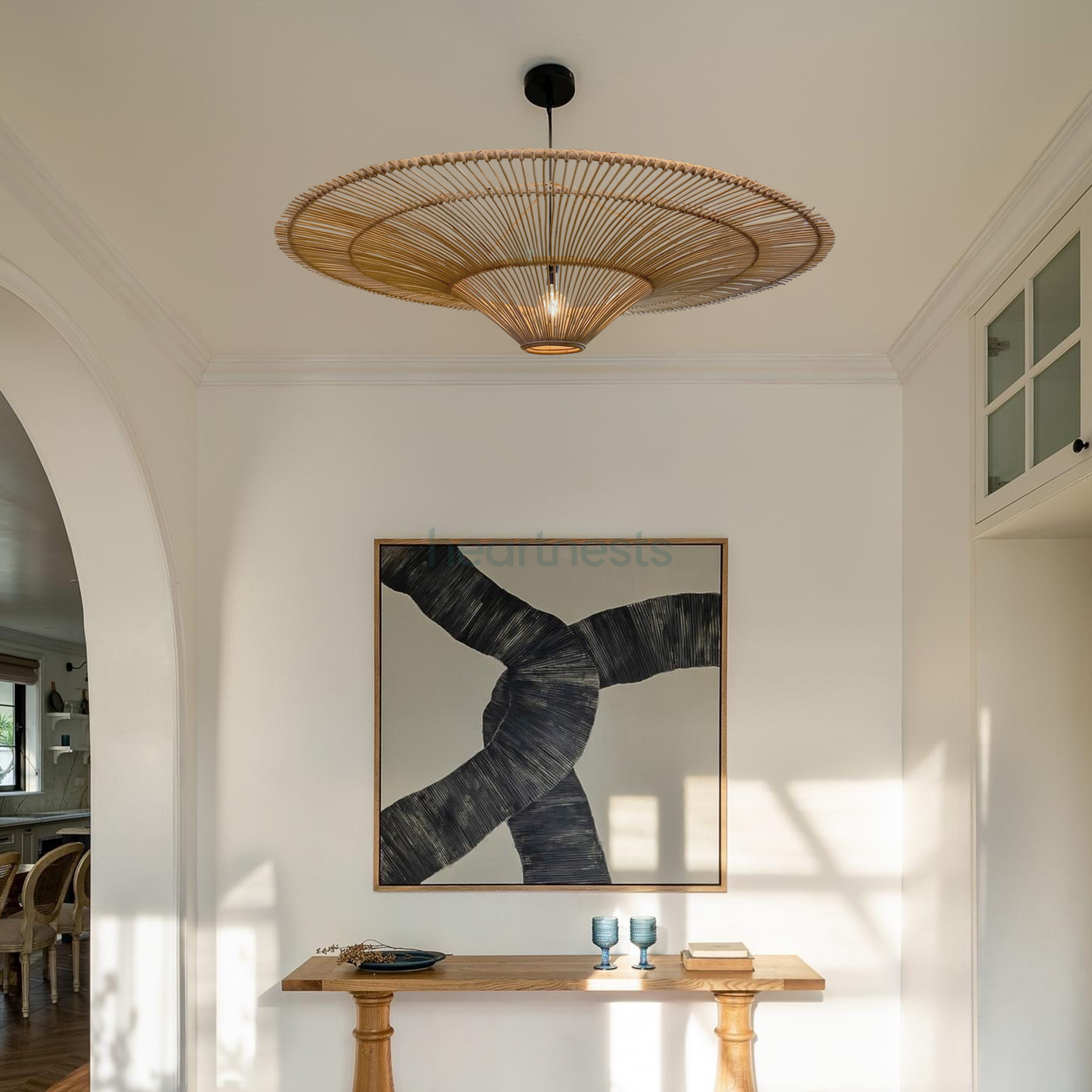 A Heartnests' Orbita Rattan Lampshade is hung above a wooden console table and a contemporary stylepainting