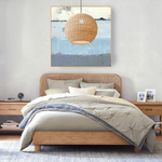 1 of Heartnests' Preethy Round Pendant Light is hung above a wooden bed and in front of an ocean painting